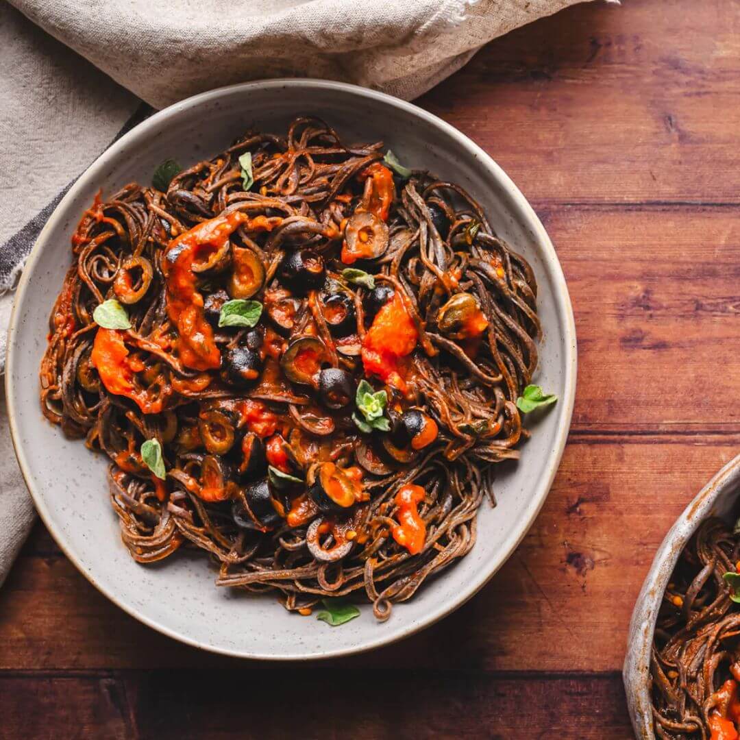 A bowl of tasty black soybean with tomato sauce and olives. 
