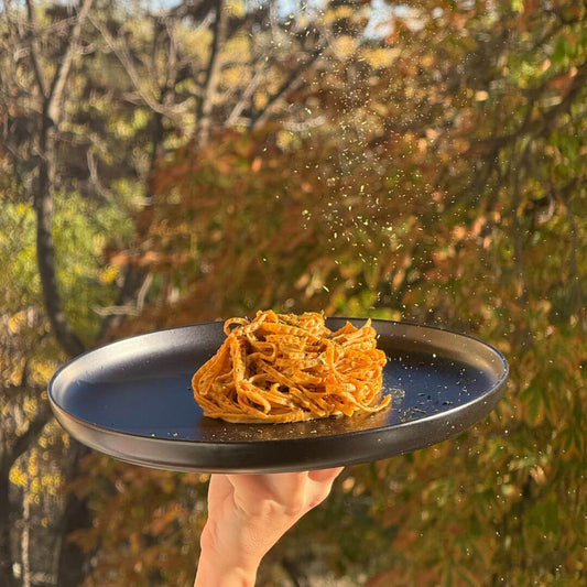 Чиния с едамаме спагети Nordama, държана на ръка на фокус, с фон от есенни дървета.