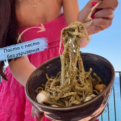 Жена държи купа с приготвени Nordama Едамаме Спагети с песто, моцарела и кашу – високопротеинова паста без глутен.